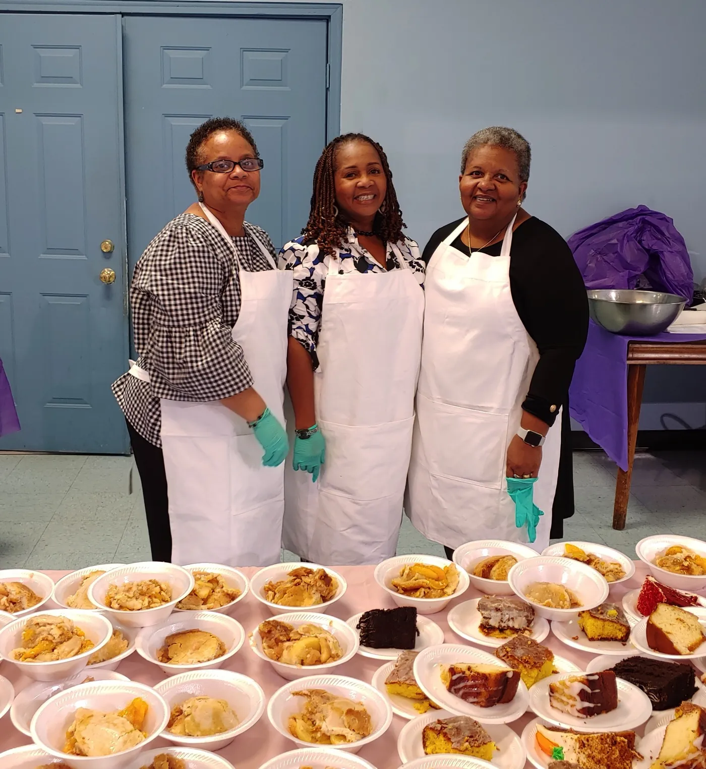 Three women of the church in aprons beside plates of food